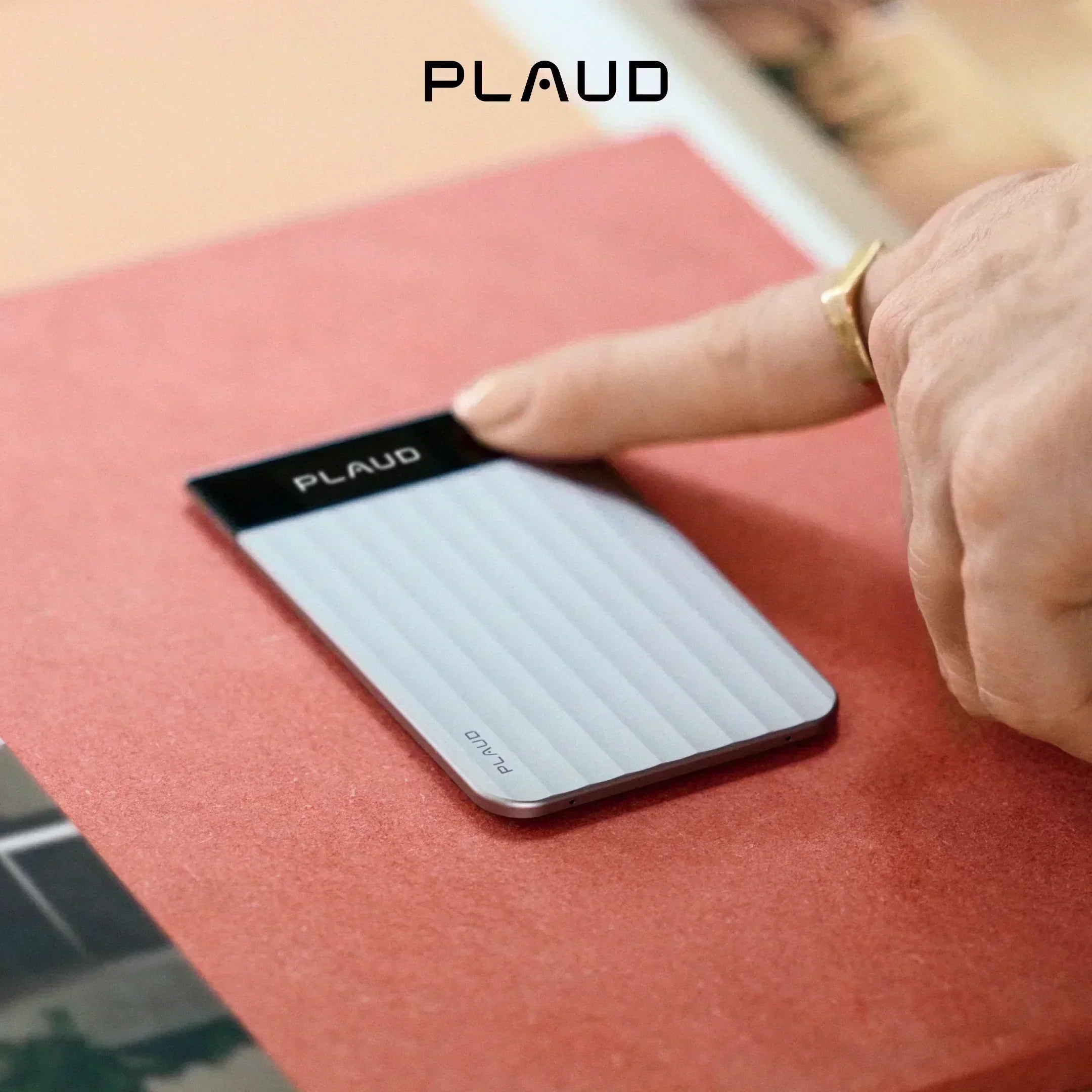 手指輕觸銀色Plaud Note Pro,置於紅棕色表面上