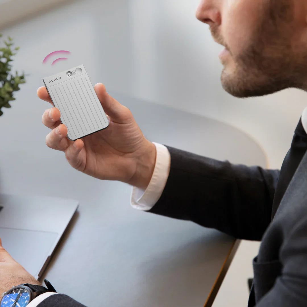 Man in a suit holding a silver Plaud Note AI voice recorder to capture a voice memo.